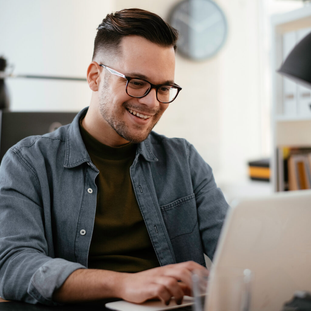 young man smiling while looking at a laptop