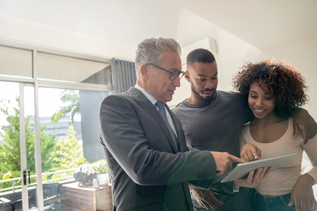 young couple with a realtor looking at a tablet device