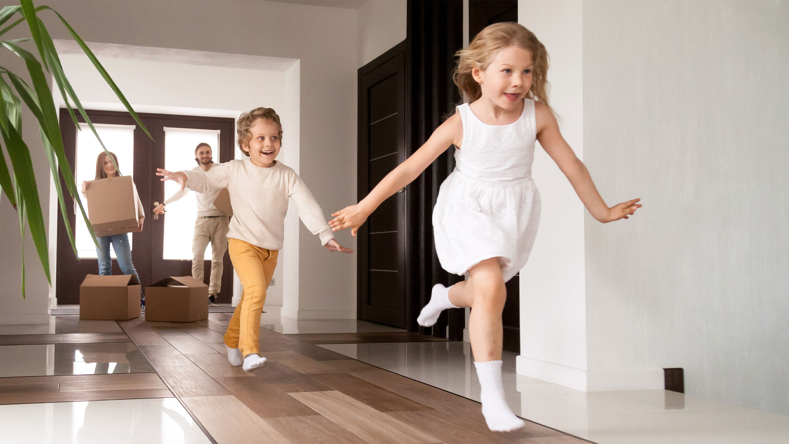 young family, with two children running and smiling after entering their new home